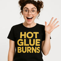 A person with curly hair styled in pigtail buns, wearing round glasses, and a black T-shirt with bold yellow text. They are smiling widely and waving with one hand.
