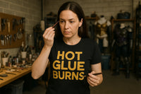 A person with long dark hair is in a workshop holding a small tool near their face, appearing focused. They are wearing a black shirt with 