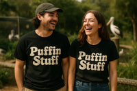 Two people are standing outdoors, smiling and laughing. They are both wearing black t-shirts that say 