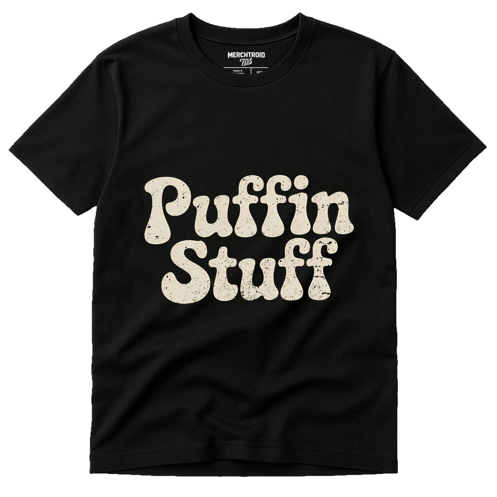 A black t-shirt featuring the words "Puffin Stuff" in large, bold, cream-colored letters across the front. The text has a slightly distressed look, giving it a vintage style. The shirt label at the neck reads "Merchtroid."