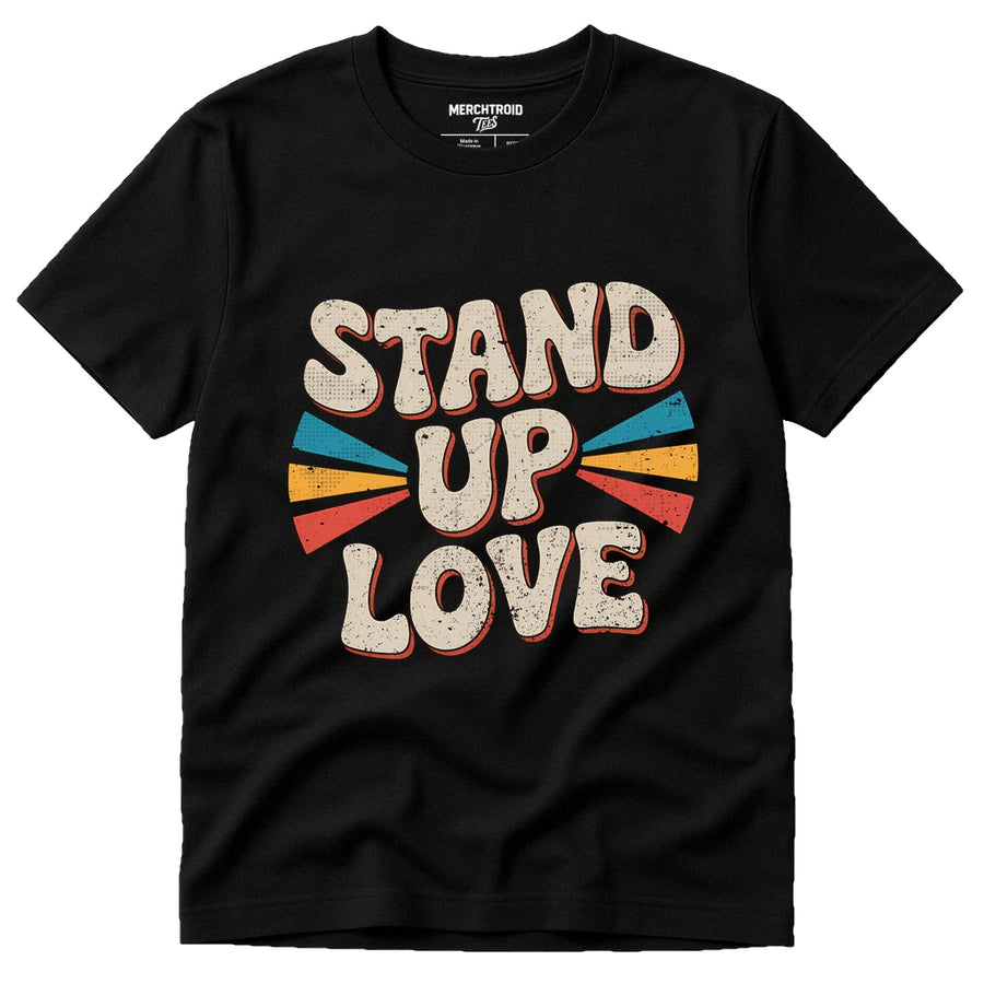 A black t-shirt with a retro-style design featuring the words "STAND UP LOVE" in bold, textured letters. The text is surrounded by colorful, fan-like shapes in red, blue, orange, and yellow.