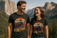 A man and woman are standing outdoors, wearing matching black t-shirts with a retro camera design and the text 