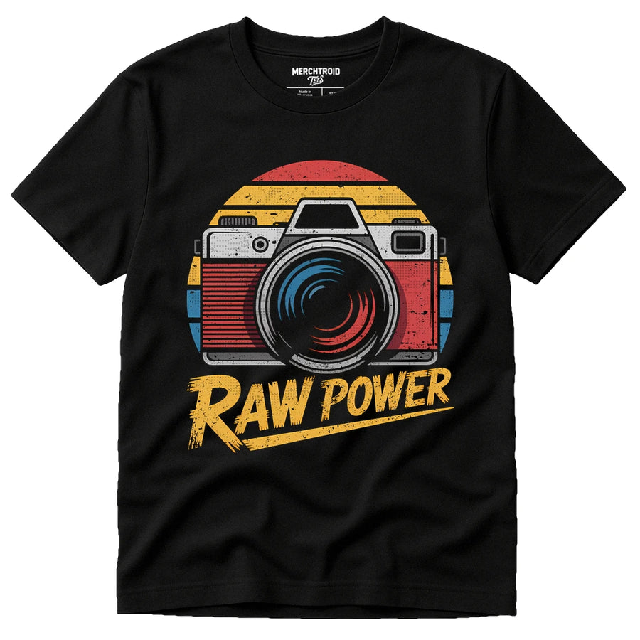 A black T-shirt featuring a vintage-style camera graphic with a sunburst background in red, yellow, and blue. The words "RAW POWER" are printed below the camera in bold, distressed yellow lettering. In the collar, the brand name "MERCHTROID" is visible.