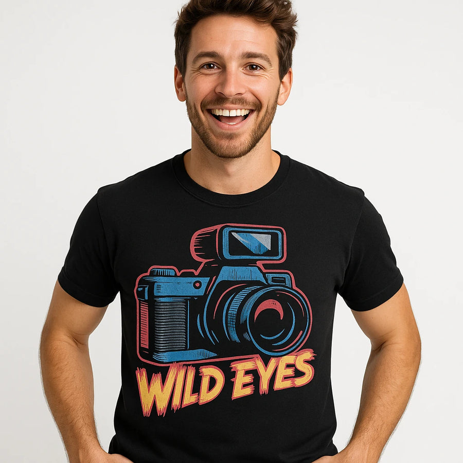 A person is smiling while wearing a black t-shirt featuring a colorful graphic of a camera above the text "WILD EYES."