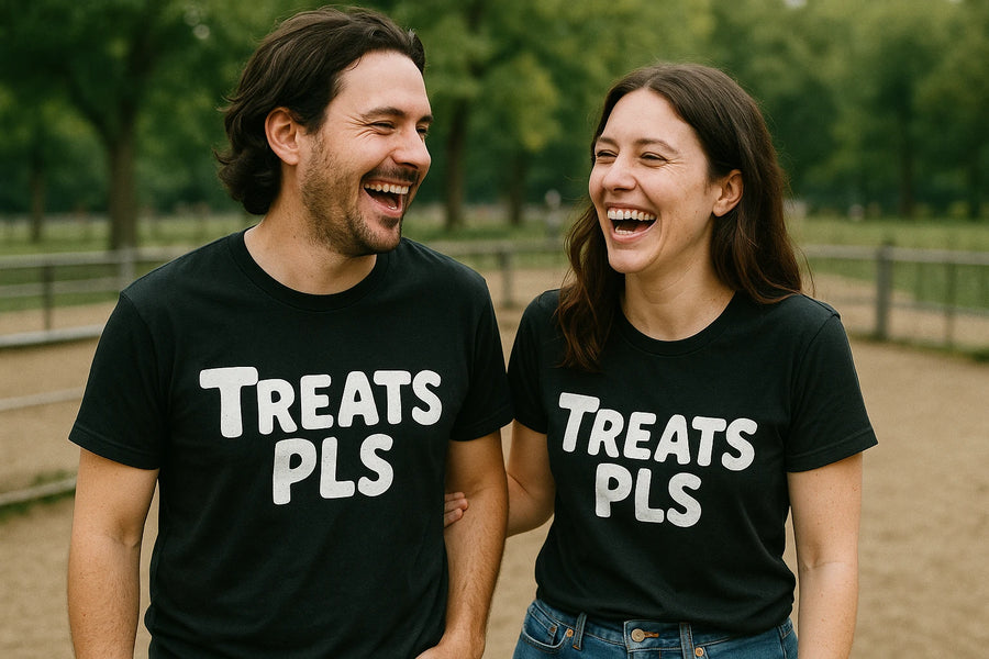 A man and a woman outdoors are laughing together while wearing matching black t-shirts with the text "TREATS PLS." The scene is set in a park-like environment with green trees in the background.