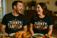 A man and a woman are seated at a dining table, both smiling and looking at each other. They are wearing matching black t-shirts with the words 