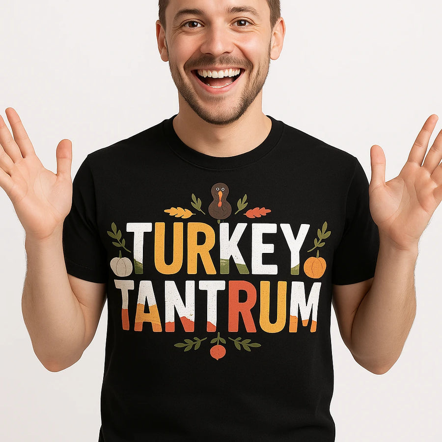 A person is smiling widely with both hands raised, wearing a black t-shirt. The shirt features colorful text that reads "TURKEY TANTRUM" with decorative elements, including a small turkey illustration and leaves. The background is plain white.