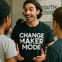 A person with long dark hair and a beard, wearing a black T-shirt with the text 