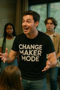A person with short brown hair is animatedly speaking while wearing a black t-shirt with the text 