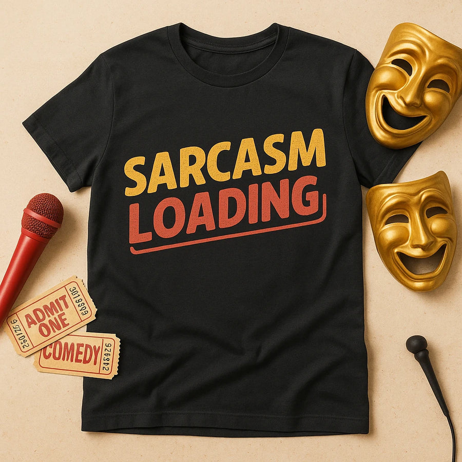 A black T-shirt is laid flat with the text "SARCASM LOADING" printed on it in bold yellow and red letters. Surrounding the shirt are two gold comedy and tragedy masks, two "Admit One Comedy" tickets, and a red microphone. The background is a neutral beige color.