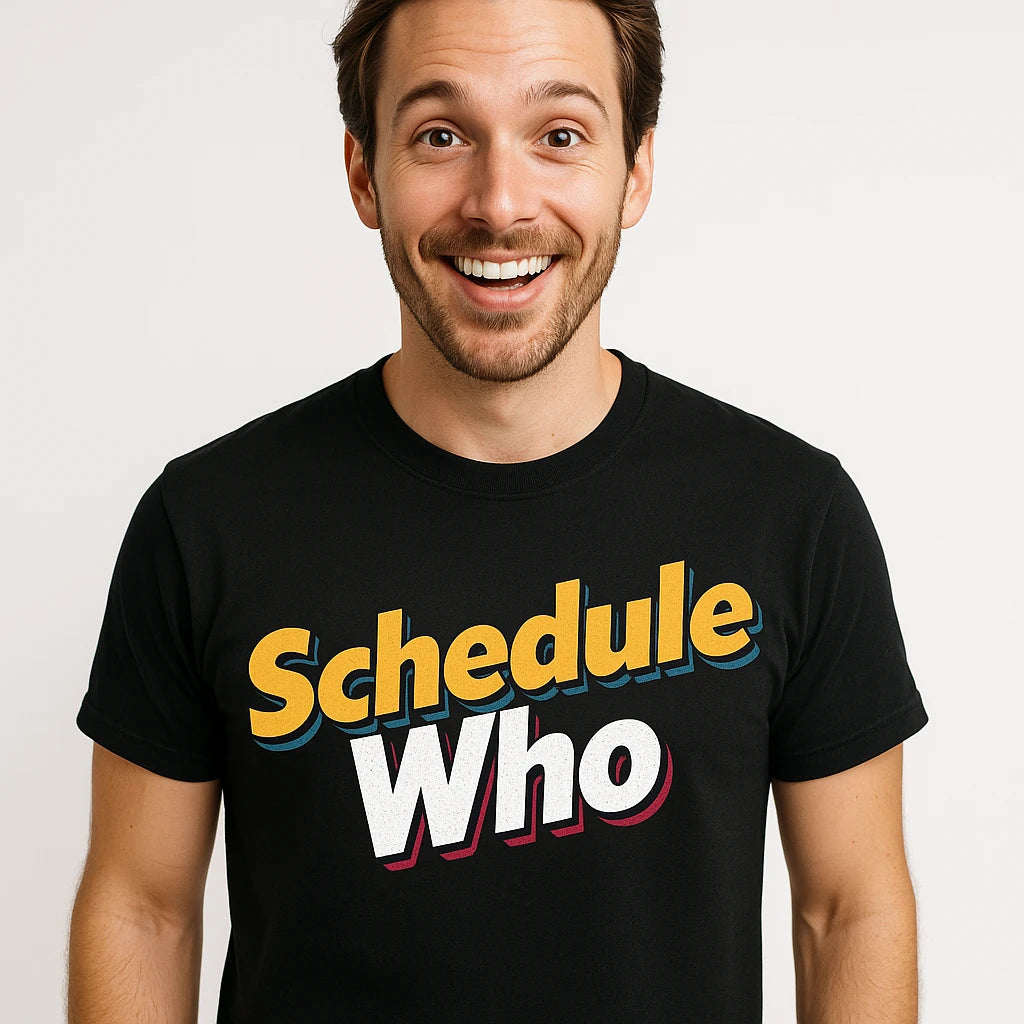 A person with short hair and a beard smiles broadly while wearing a black t-shirt with colorful text that reads "Schedule Who". The background is plain white.