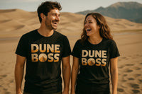 A man and a woman are standing on sand dunes, both wearing black T-shirts with the text 