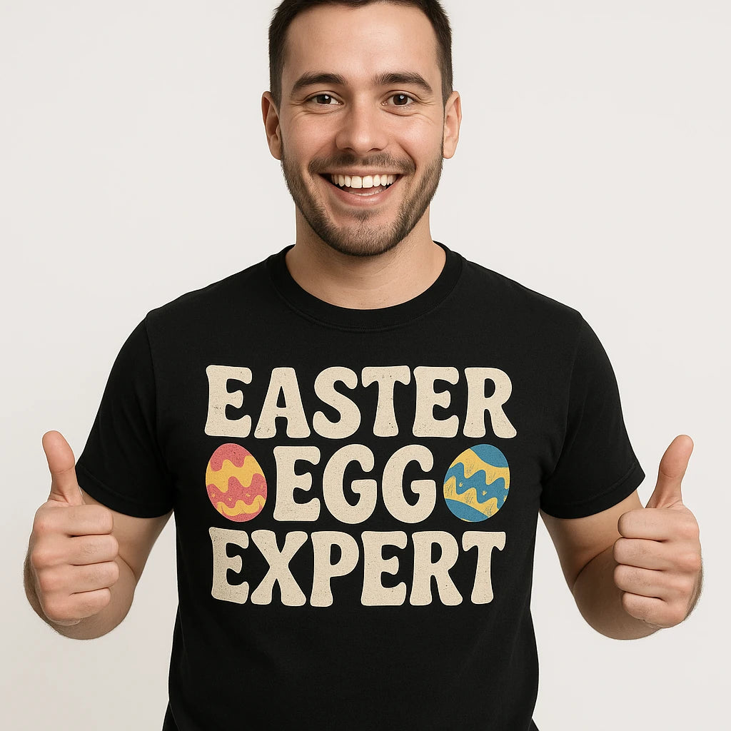 A smiling person with short dark hair is giving two thumbs up. They are wearing a black t-shirt with the text "EASTER EGG EXPERT" and images of decorated Easter eggs.