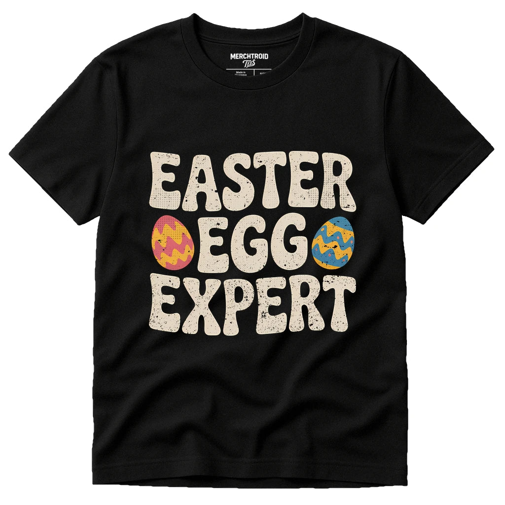 A black T-shirt featuring the slogan "EASTER EGG EXPERT" in large, bold white letters, with colorful Easter eggs integrated into the letters "E" and "G".