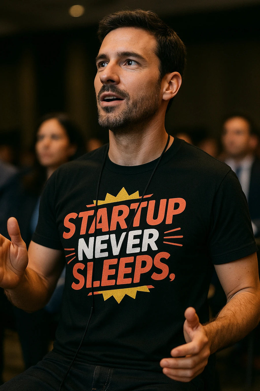 A person wearing a black t-shirt with bold red and white text that reads "STARTUP NEVER SLEEPS." They have a thoughtful expression, and there's a conference ambiance with blurred people in the background.