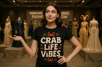 A person with brown hair, smiling slightly, stands in a fashion exhibit room. They are wearing a black t-shirt with the text 