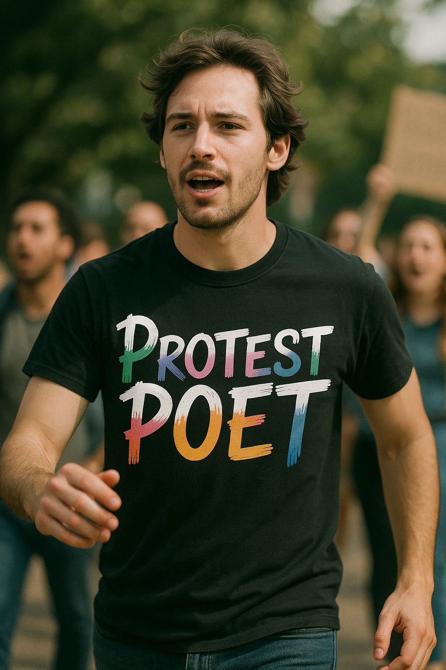 A person with medium-length dark hair is wearing a black T-shirt with the words "PROTEST POET" in colorful, artistic letters. The person appears to be part of a group of people, possibly at a rally or protest, with others blurred in the background.