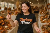 A person with dark hair is smiling while holding a pine cone with small red berries. They are wearing a black shirt with the text 