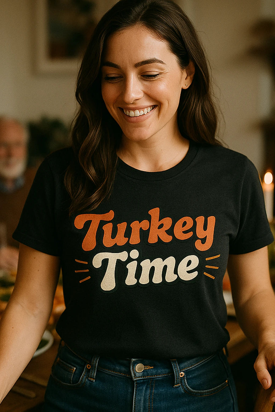 A woman with long, dark hair is smiling while wearing a black T-shirt with the words "Turkey Time" in festive colors. She appears to be indoors, possibly in a dining setting.