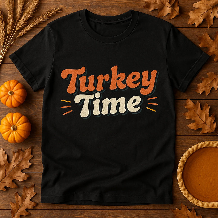 A black t-shirt with the text "Turkey Time" printed in bold, stylish letters. The background is decorated with autumn-themed items, including small pumpkins, dried wheat stalks, and orange-brown leaves, arranged on a wooden surface. There is also a pumpkin pie visible, enhancing the fall and Thanksgiving theme.