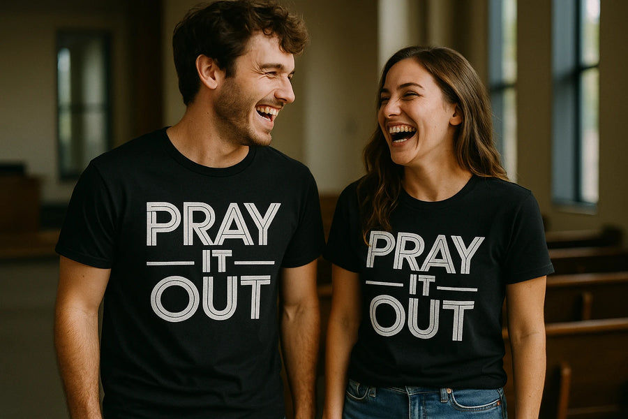 A man and a woman are standing side by side, smiling and looking at each other. They are both wearing matching black T-shirts with the text "PRAY IT OUT." The background indicates they might be in a church or similar setting, with pews and large windows visible.