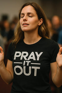 A person with long brown hair is standing with their eyes closed, appearing to be in a moment of meditation or prayer. They are wearing a black T-shirt with the words 
