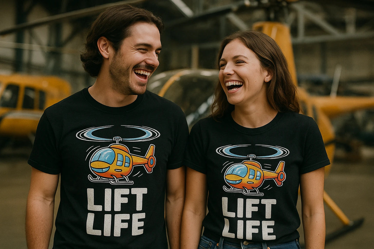 A man and a woman are standing side by side, both wearing black T-shirts featuring a cartoon helicopter and the text "LIFT LIFE." They are smiling and appear to be sharing a moment of laughter. Helicopters are visible in the background, suggesting they might be in a hangar or aviation-related setting.
