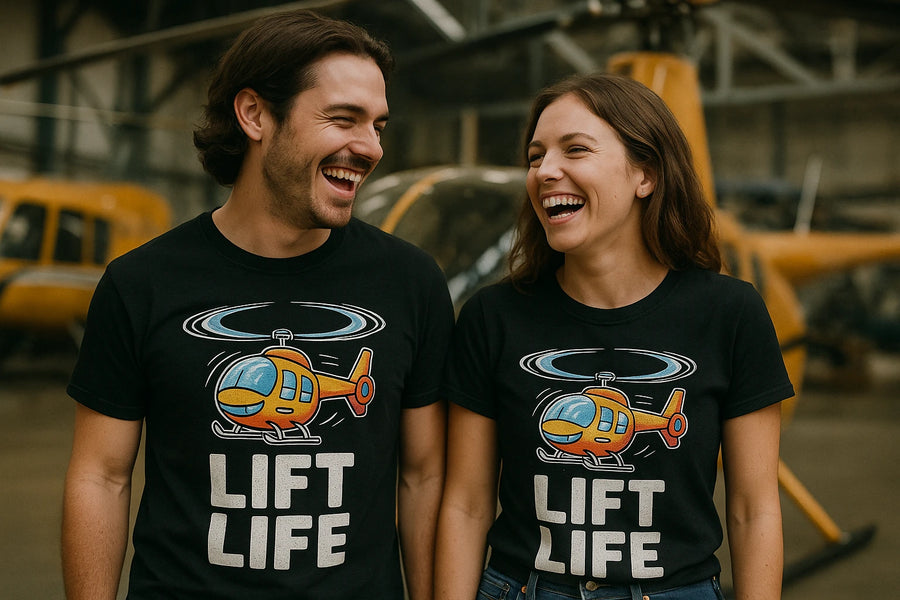 A man and a woman are standing side by side, both wearing black T-shirts featuring a cartoon helicopter and the text "LIFT LIFE." They are smiling and appear to be sharing a moment of laughter. Helicopters are visible in the background, suggesting they might be in a hangar or aviation-related setting.
