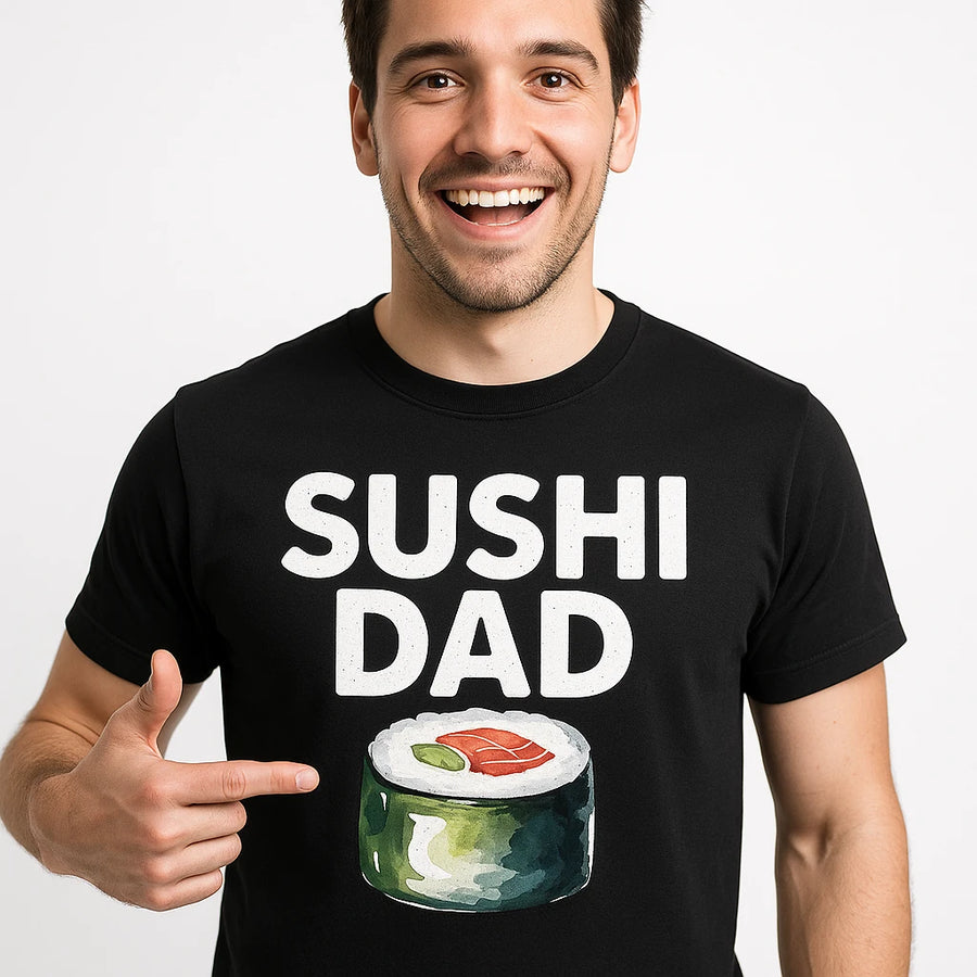 A person wearing a black t-shirt with the text "SUSHI DAD" and an illustration of a sushi roll. The person is smiling broadly and pointing at the design on their shirt. The background is plain white.