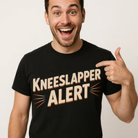 A person with a beard and short hair is smiling broadly and pointing at their black T-shirt with the text 