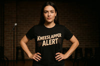 A person with long dark hair stands confidently with their hands on their hips, wearing a black t-shirt that says 