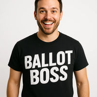 A smiling person with short dark hair and a beard is wearing a black T-shirt with the words 