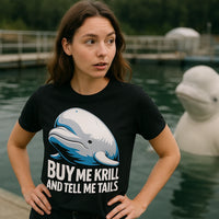 A person with long brown hair is standing near a body of water, wearing a black T-shirt featuring a cartoon beluga whale and the text 