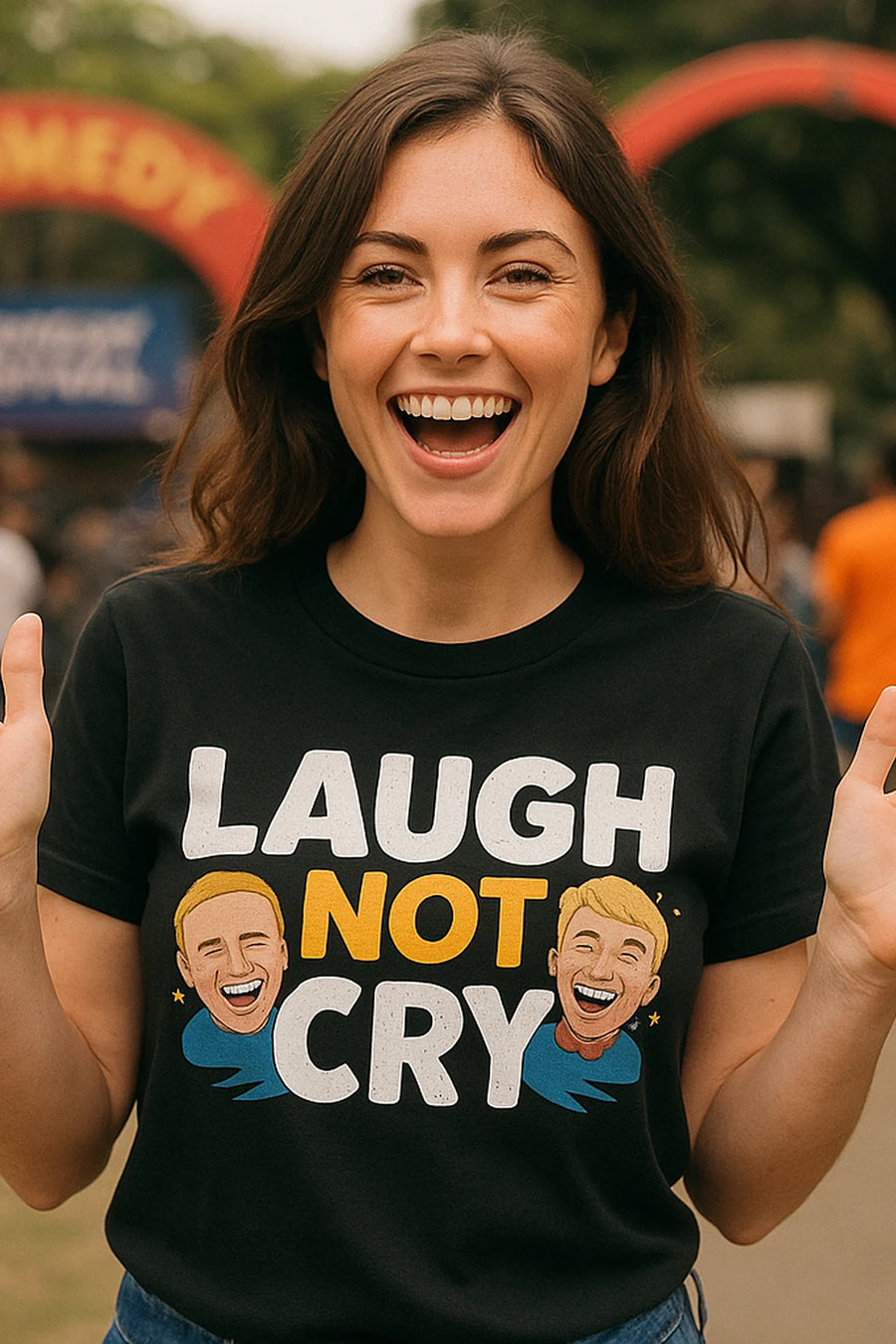 A person with long brown hair, wearing a black t-shirt with the text "LAUGH NOT CRY" and illustrations of smiling faces. They are outdoors, smiling broadly, with an arch and blurred people in the background.