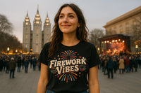 A person stands outdoors at a festive event, wearing a black T-shirt with colorful fireworks and the text 