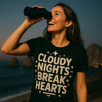 A person is smiling while looking through binoculars. They are wearing a black T-shirt with the text 