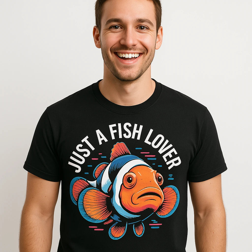 A person wearing a black t-shirt with a colorful illustration of a clownfish below the text "Just A Fish Lover." The person is smiling widely and standing against a plain white background.