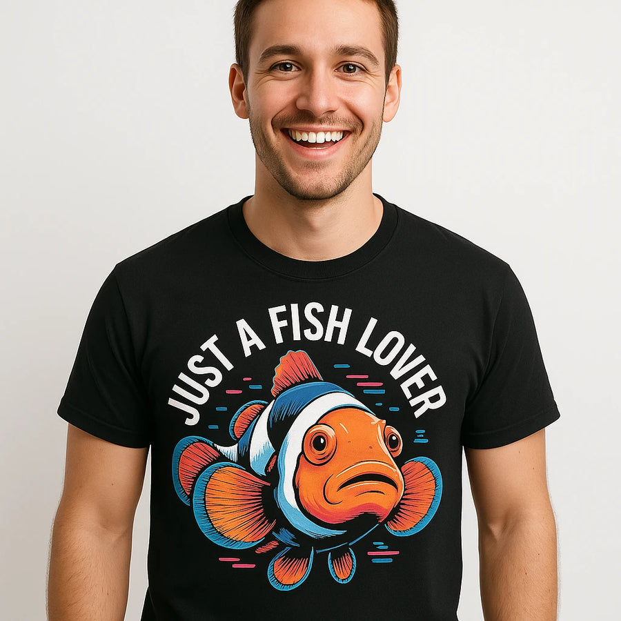 A person wearing a black t-shirt with a colorful illustration of a clownfish below the text "Just A Fish Lover." The person is smiling widely and standing against a plain white background.