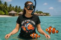 A person with a snorkel and mask stands in clear tropical water, wearing a black t-shirt with an illustration of a clownfish and the text 
