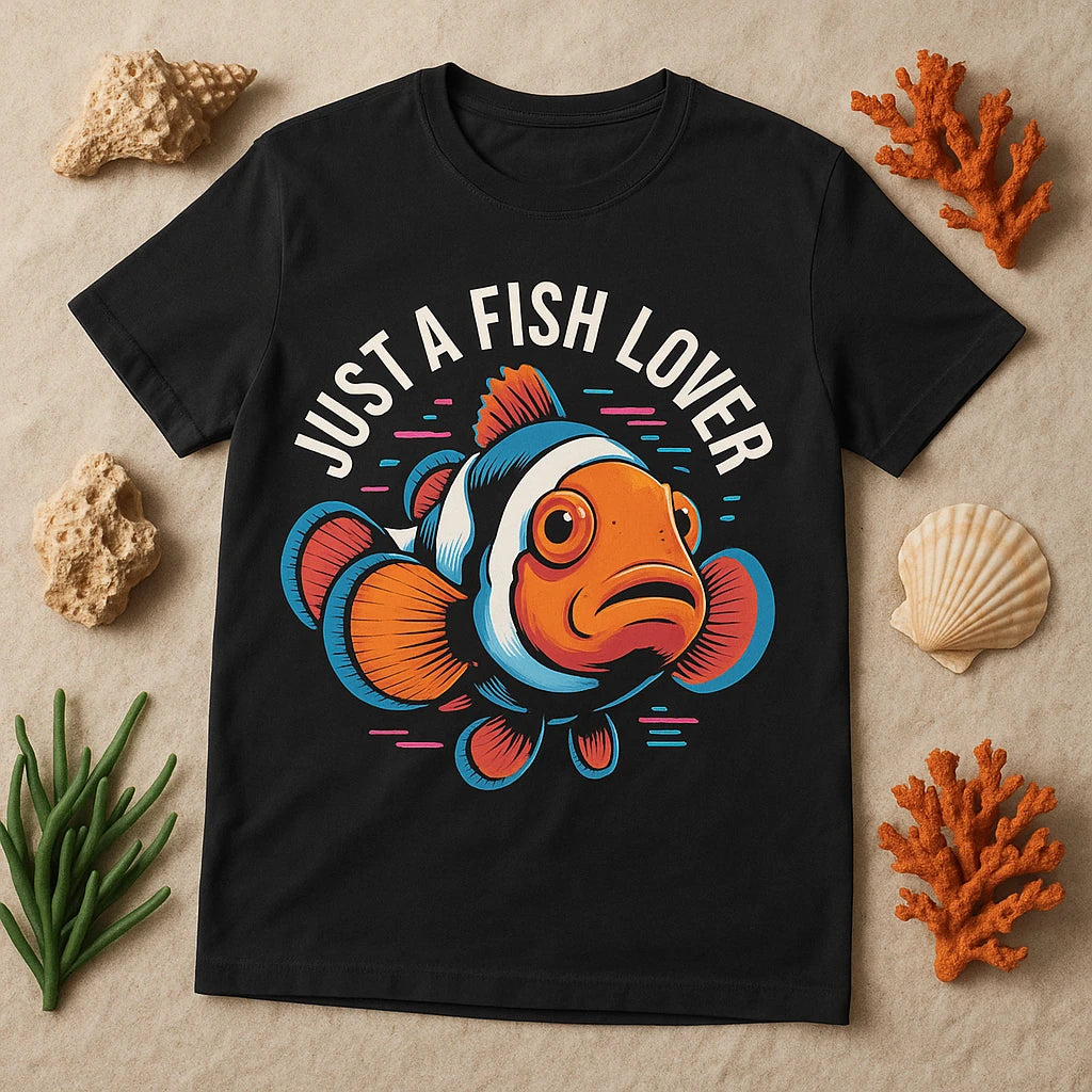 A black T-shirt featuring a colorful illustration of a clownfish with the text "JUST A FISH LOVER" above it. The shirt is surrounded by coral, seashells, and aquatic plants, enhancing the marine theme.