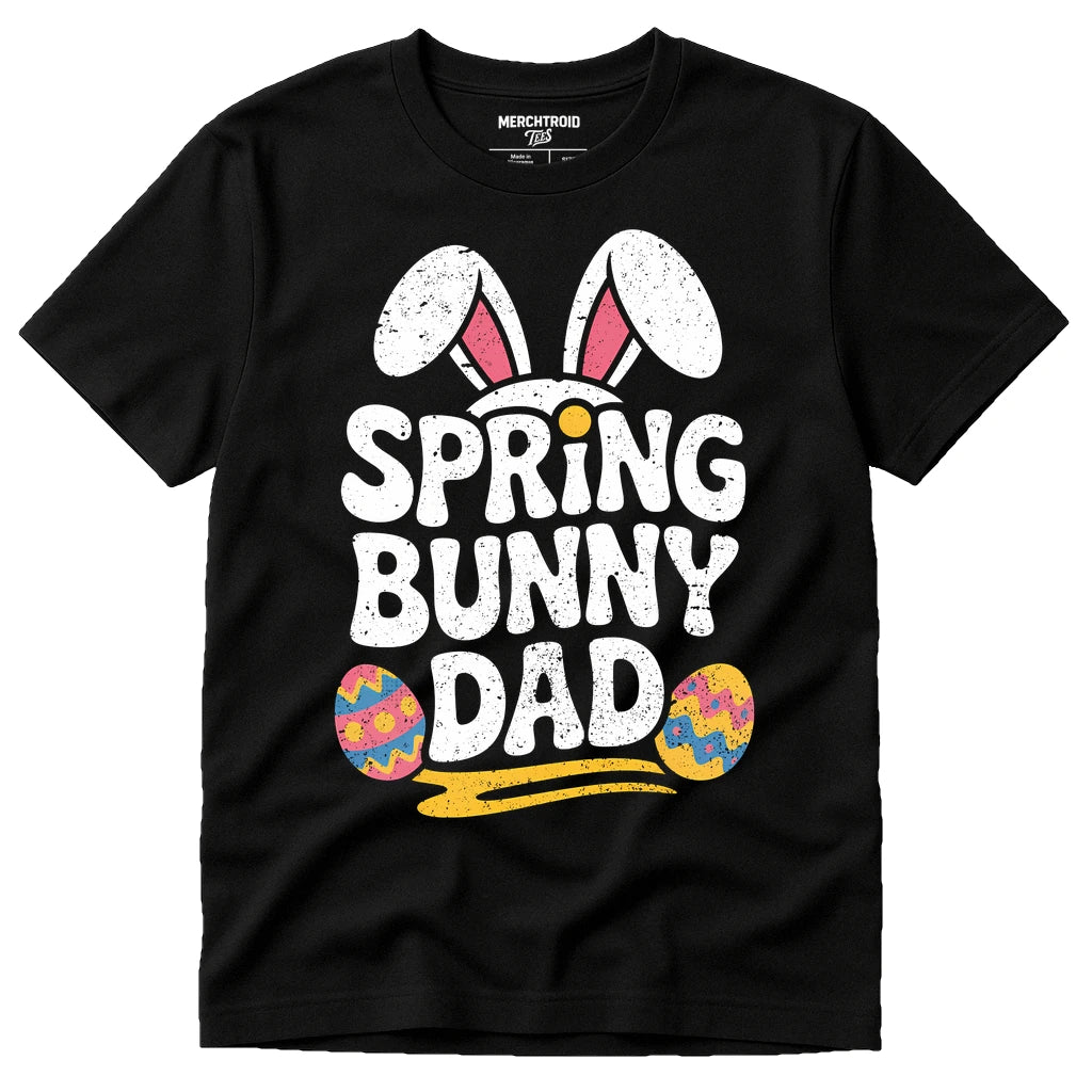 A black t-shirt featuring the text "SPRING BUNNY DAD" in bold, white letters with bunny ears and two colorful Easter eggs for decoration.