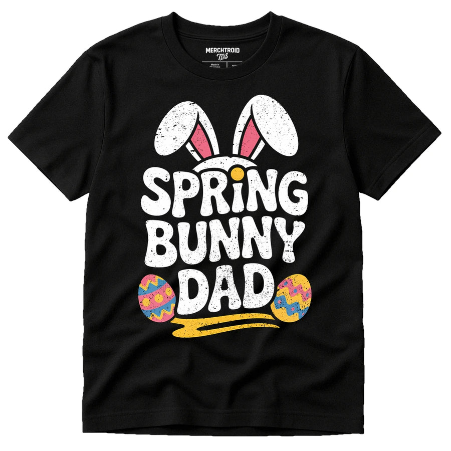 A black t-shirt featuring the text "SPRING BUNNY DAD" in bold, white letters with bunny ears and two colorful Easter eggs for decoration.