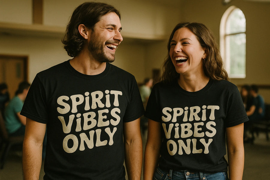 A man and a woman are standing side by side, smiling and laughing. Both are wearing black T-shirts with the text "SPiRiT VIBES ONLY" in bold, cream-colored letters. The background shows a room with other people blurred in the distance, suggesting a social or casual setting.