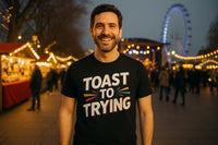 A person with a beard is smiling and wearing a black T-shirt with the text 