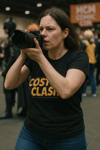 A person with long brown hair is taking a photograph with a camera. They are wearing a black T-shirt with the text 