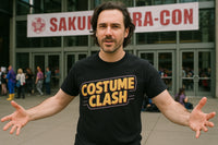 A person with medium-length brown hair and facial hair is wearing a black t-shirt with 