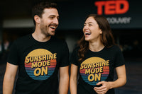 A man and a woman are smiling and laughing together, both wearing black t-shirts with the text 