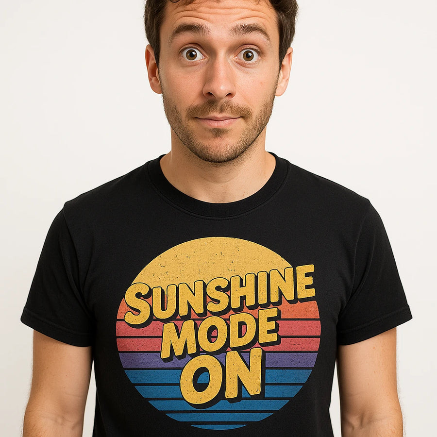 A person with short dark hair and a surprised expression is wearing a black t-shirt with a graphic featuring a retro-style sunset and the text "SUNSHINE MODE ON."
