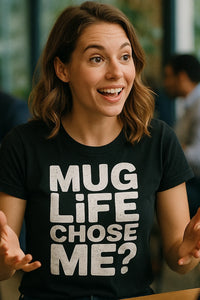 A person with shoulder-length brown hair is smiling and animatedly using their hands. They are wearing a black t-shirt with bold white text. The background is blurred, showing an indoor environment.
