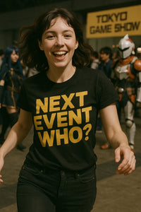 A person with dark hair is smiling energetically at the camera. They are wearing a black t-shirt with bold yellow text that reads 